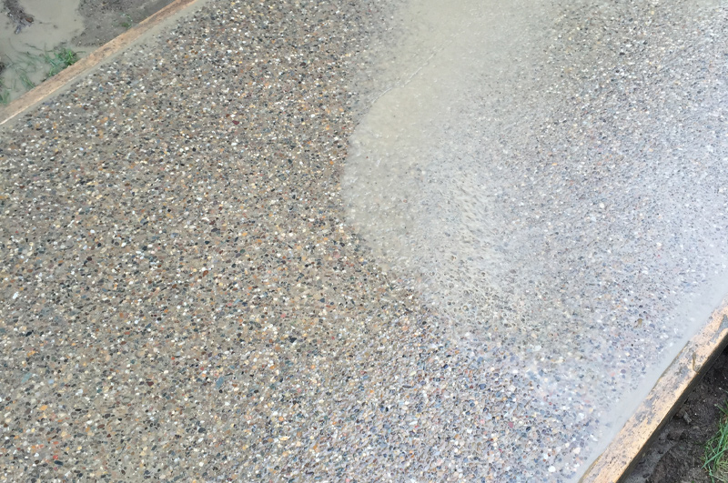 Cream finish being washed from an exposed aggregate concrete sidewalk in Schoolcraft, Michigan